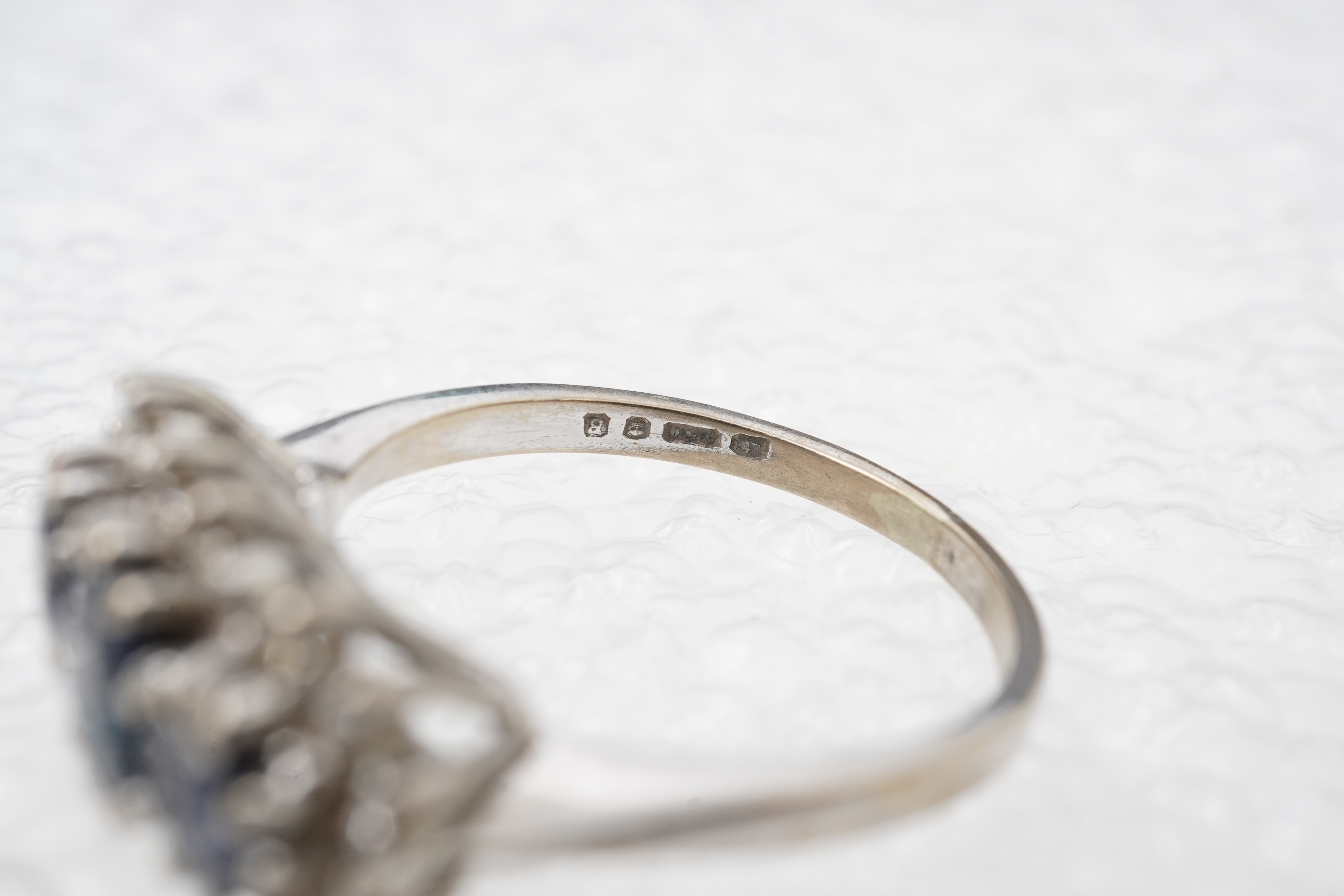 A sapphire and diamond ring, set with three circular-cut and oval sapphires, within a border of brilliant-cut diamonds totalling approximately 0.40 carats, mounted in 18ct white gold, size M1/2, British hallmarks, gross